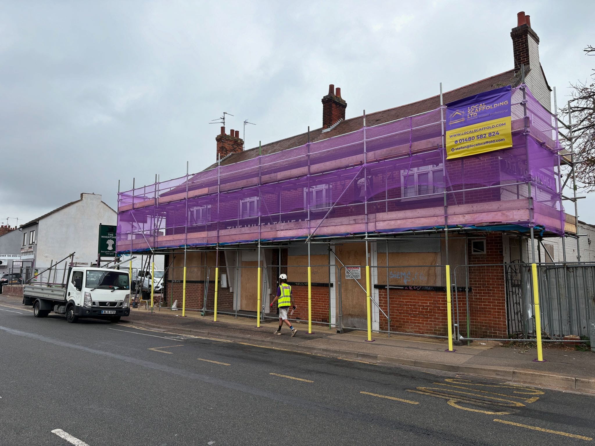 Full-frontage commercial scaffold with purple debris netting wrapping a pub building during renovation works